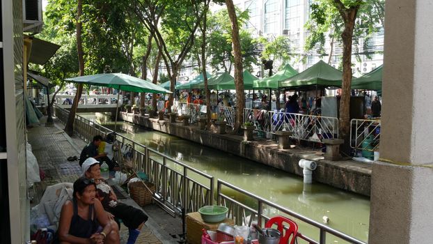 BANGKOK, THAILAND - 11 JULY, 2019: Street city life near river canal in siam. Traditional khlong with bridge near local market. Thai people on the riverside. Classic water way in Krungtep