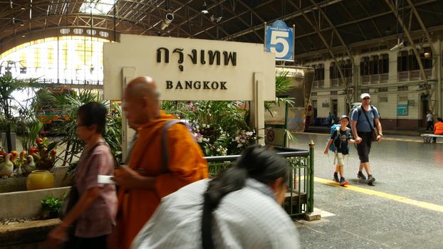 BANGKOK, THAILAND - 11 JULY 2019: Hua Lamphong railroad station, state railway transport infrastructure SRT. Buddhist holy Monk in traditional orange robe. Monks yellow religious clothes among people