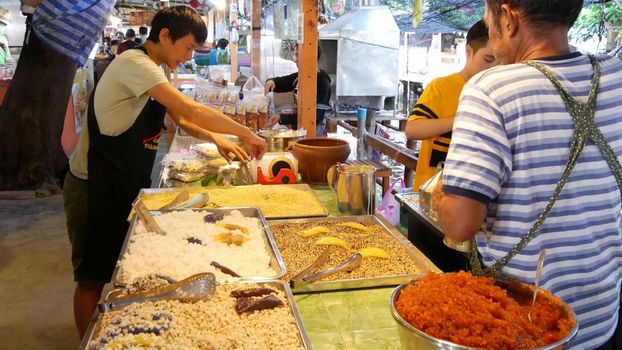 BANGKOK, THAILAND - 13 JULY 2019: Lat Mayom khlong river canal traditional classic floating market. Iconic local asian street food selling. Sellers and buyers at the counters with exotic goods.