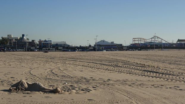 SANTA MONICA, LOS ANGELES CA USA - 19 DEC 2019: Alone anonymous man looks like unemployed and homeless sleeping on beach sand. Homelessness and begging crisis, social issue, poor people live on street