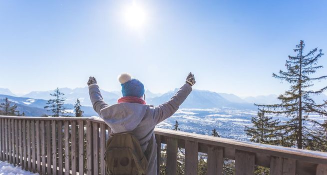 Back of young woman who is raising her hands on the mountain, outlook. Gaisberg, Austria