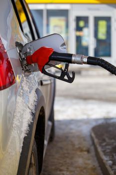 silver metallic car refueling on winter day gas station - close-up with selective focus and blurry background.