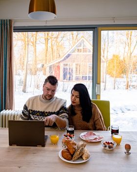 Young couple morning breakfast with laptop.Love,happiness,people and fun working from home concept. young couple mid age Asian and Causian man and woman working from home with laptop