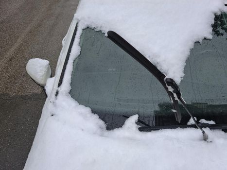 Day view of frozen windshield blade raised up above a parked vehicle on a cold winter day.