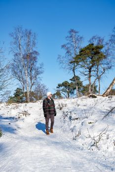 man mid age walking in the snow, snow covered hills of the Sallandse Heuvelrug, Landscapes of the Holterberg near Holten, The Netherlands. Winter in the Netherlands