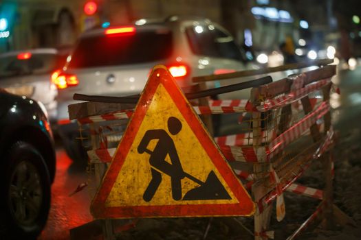 Road works ahead sign at winter night street near pit - close-up with selective focus