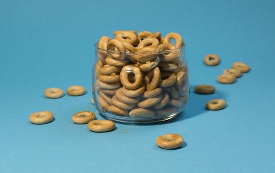 Yellow small sushki bagels in glassware on a blue background. Bagels are scattered around