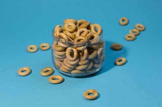 Yellow small sushki bagels in glassware on a blue background. Bagels are scattered around