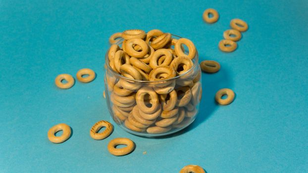 Yellow small sushki bagels in glassware on a blue background. Bagels are scattered around