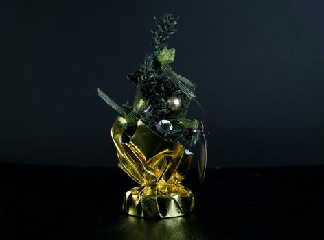 Small Christmas tree in a bag with decorations. Table accessory with gold decor. Christmas tree on black background for greeting cards