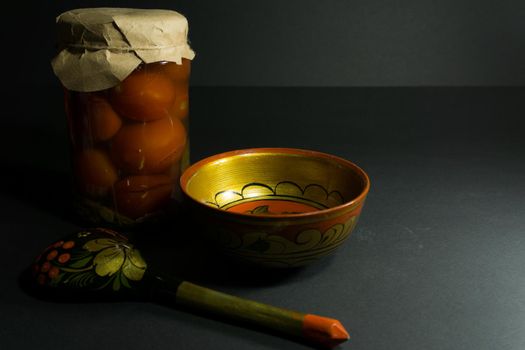 Jar of pickled tomatoes, a spoon with folk painting and a wooden bowl