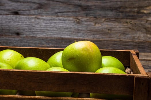 Wooden crate with ripe green apples on wooden table.