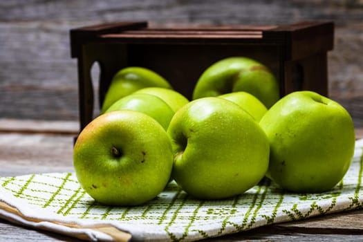 Wooden crate with ripe green apples on wooden table.