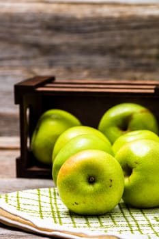 Wooden crate with ripe green apples on wooden table.