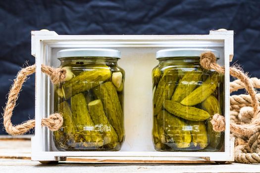 Wooden crate with glass jars with pickles isolated. Preserved food concept, canned vegetables isolated in a rustic composition.