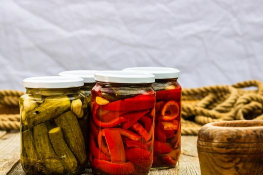 Glass jars with pickled red bell peppers and pickled cucumbers (pickles) isolated. Jars with variety of pickled vegetables. Preserved food concept in a rustic composition.