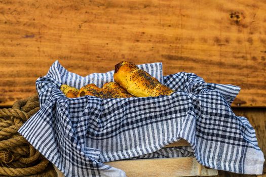 Sausages baked in dough sprinkled with salt and poppy seeds in a rustic composition. Sausages rolls, delicious homemade pastries.