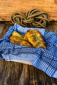 Sausages baked in dough sprinkled with salt and poppy seeds in a rustic basket. Sausages rolls, delicious homemade pastries in a rustic composition.