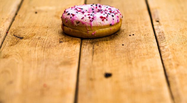 Colorful donuts on wooden table. Sweet icing sugar food with glazed sprinkles, doughnut with chocolate frosting. Top view with copy space