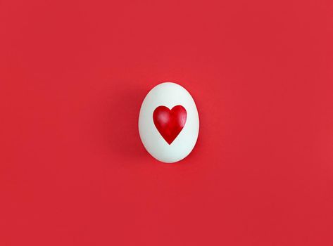 White egg with heart shape on a red background.