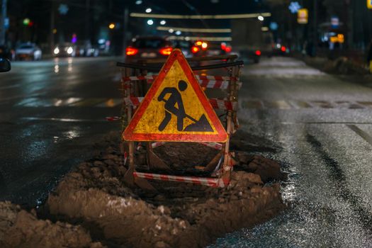 Road works ahead sign at winter night street near pit - close-up with selective focus