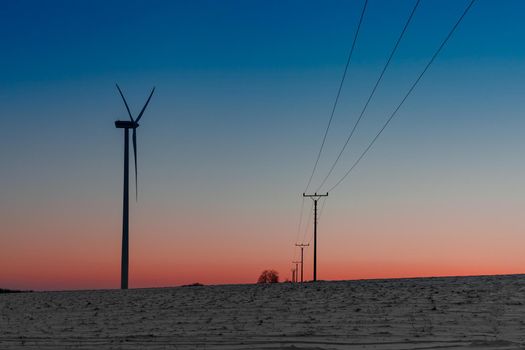 wind power plant in the field next to a power line at sunset.