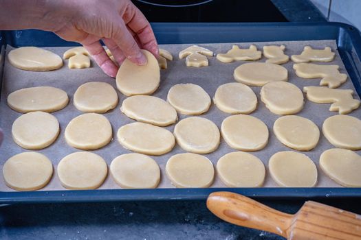  Woman prepares butter cookies at home in the kitchen, the table is sprinkled with flour, rolls out the dough, cuts out the shape, the concept of cooking festive food, christmas or easter sweets