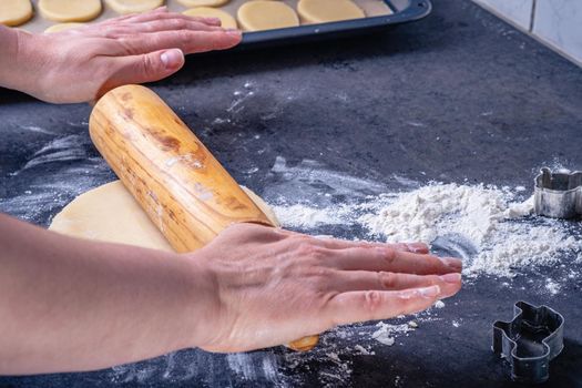 Woman prepares butter cookies at home in the kitchen, the table is sprinkled with flour, rolls out the dough, cuts out the shape, the concept of cooking festive food, christmas or easter sweets