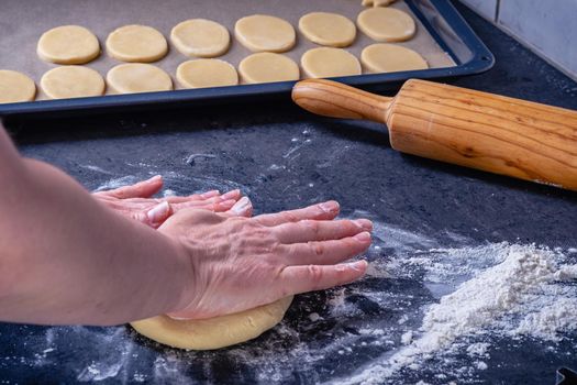  Woman prepares butter cookies at home in the kitchen, the table is sprinkled with flour, rolls out the dough, cuts out the shape, the concept of cooking festive food, christmas or easter sweets