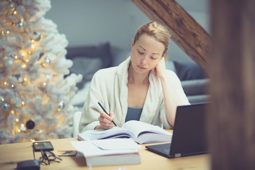 Young businesswoman wearing cosy warm bathrobe working remotly from home in winter Christmas time during 2020 corona virus pandemic. Work from home, selter in place, concept.