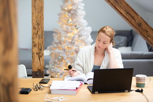 Young businesswoman wearing cosy warm bathrobe working remotly from home in winter Christmas time during 2020 corona virus pandemic. Work from home, selter in place, concept.