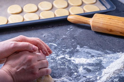  Woman prepares butter cookies at home in the kitchen, the table is sprinkled with flour, rolls out the dough, cuts out the shape, the concept of cooking festive food, christmas or easter sweets