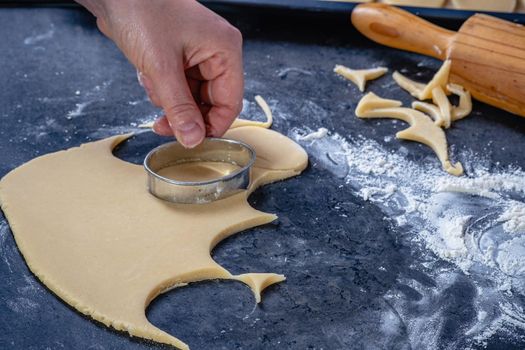 Woman prepares butter cookies at home in the kitchen, the table is sprinkled with flour, rolls out the dough, cuts out the shape, the concept of cooking festive food, christmas or easter sweets