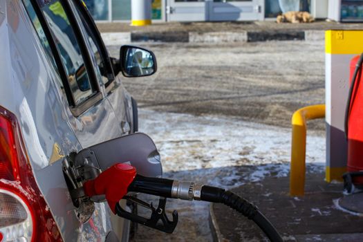 silver metallic car refueling on winter day gas station - close-up with selective focus and blurry background.