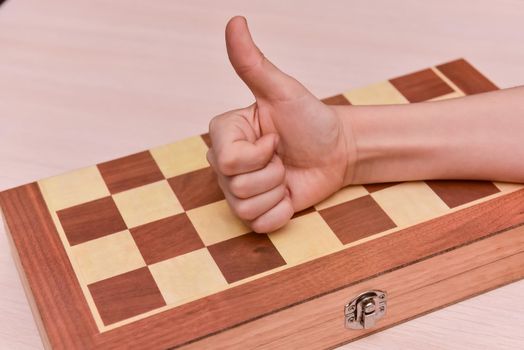 child's hand on the chessboard showing thumb up. cool game at home.