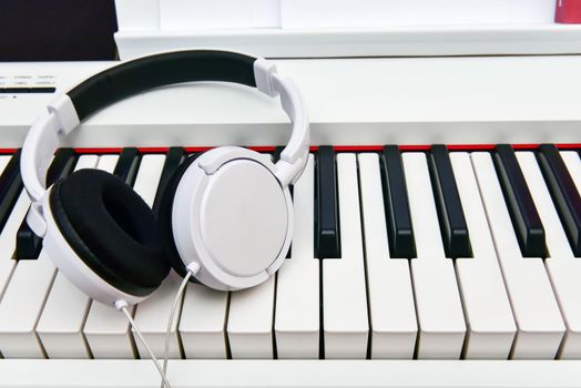 white headphones lie on the keyboard of the electronic piano.
