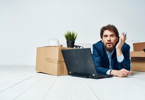 A man in a suit lies on the floor with office boxes unpacking a laptop technology. High quality photo