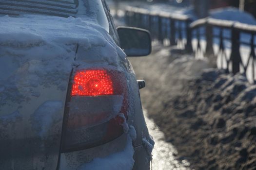 dirty car tail light with snow at winter evening with dirty blurry snowdrift in the background