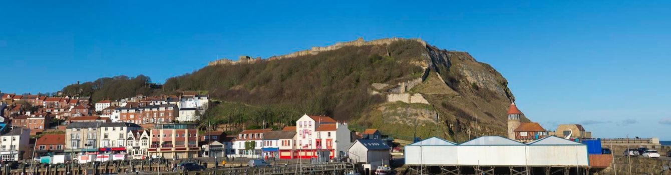 Landscape panorama view of coastal seaside town harbor front with medieval castle on hill headland