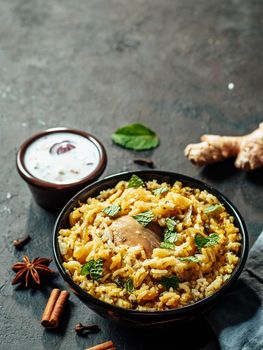 Pakistani food - biryani rice with chicken and raita yoghurt dip. Delicious hyberabadi chicken biryani on black background. Copy space for text. Vertical