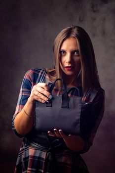 A beautiful girl holds a handbag in front of her and looked into the frame with big eyes