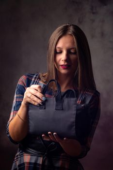 A beautiful girl holds a handbag in front of her and mysteriously opens it