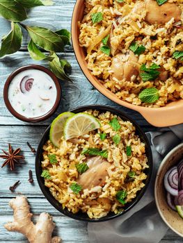 Pakistani food - biryani rice with chicken and raita yoghurt dip. Delicious hyberabadi chicken biryani on gray wooden background. Top view or flat lay. Copy space. Vertical.