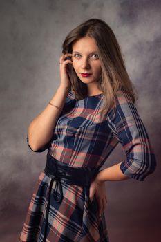 Portrait of a beautiful girl in an interesting checkered dress on a gray background