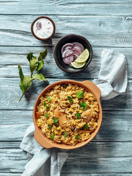 Pakistani food - biryani rice with chicken and raita yoghurt dip. Delicious hyberabadi chicken biryani on gray wooden background. Top view or flat lay. Copy space. Vertical.