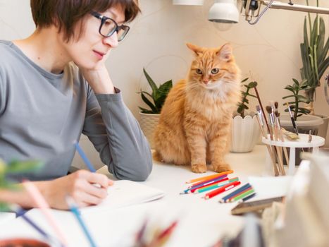 Woman with short hair cut is drawing in notebook. Cute ginger cat sits near her. Fluffy pet and artist. Calming hobby, anti stress leisure.