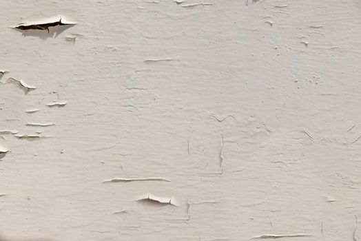 Outdoors, beige paint flakes off the surface of the wall in close-up.Texture or background