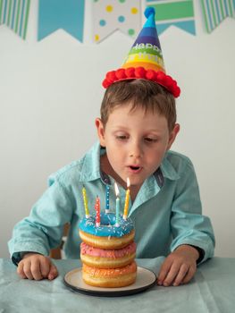 Five year old boy blows out the candles on festive donuts cake in his birthday. Happy little child and plate with doughnuts stack cake with candles on the table. Vertical.