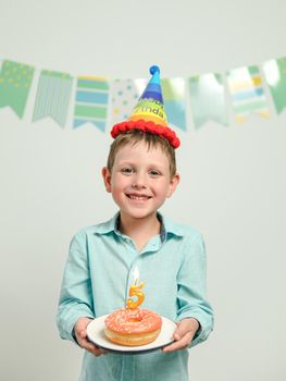 Five year old boy in his birthday with festie donut. Happy little child hold plate with doughnut with candle and looking at camera