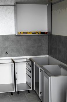 Custom kitchen cabinets installation without a furniture facades mdf. Gray modular kitchen from chipboard material on a various stages of installation in kitchen with a grey tile on floor and walls